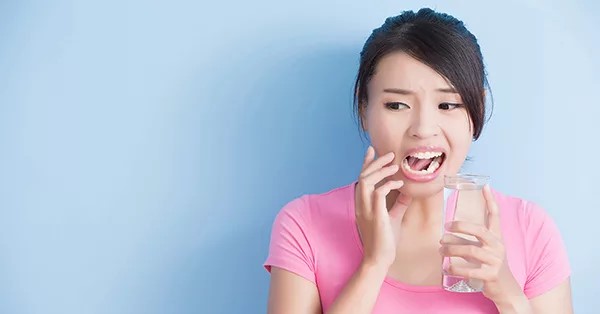 Cách giảm ê buốt tại nhà trong lúc chờ khám là súc miệng nước muối ấm,